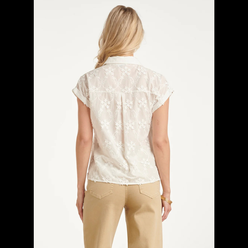 Blusa branca de manga curta, adornada com um padrão floral delicado em detalhes de bordado refinado. Fechamento frontal com botões.