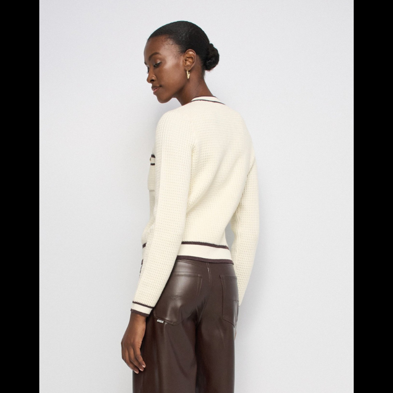 Cardigan versátil em tom bege com elegantes rebordos castanhos. Corte slim ajustado que valoriza a silhueta, mangas compridas e abertura frontal com botões dourados que adicionam um toque sofisticado. Os bolsos no peito reforçam a estética inspirada no tailoring francês.