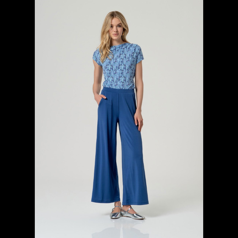 Camisola de manga curta em azul com decote a barco e drapeado elegante num ombro. Apresenta um padrão sofisticado que combina riscas verticais com motivos florais, criando um visual dinâmico e feminino. Confecionada em viscose EcoVero e elastano, oferece conforto e flexibilidade, com a vantagem de ser uma escolha sustentável. Perfeita para looks casuais ou mais elaborados.