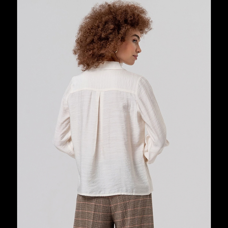 Camisa de manga comprida em crú fluida com gola e botões na frente. Ombros com franzidos que dão volume e punhos bufantes.