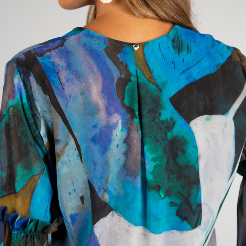 Túnica de decote em V com estampado abstrato em tons de turquesa, azul e verde. Túnica de mangas compridas em formato balão, levemente transparentes e forrada no corpo. Mangas a terminar com punho alto com dois botões metálicos em relevo.
Composição: 100%Poliester