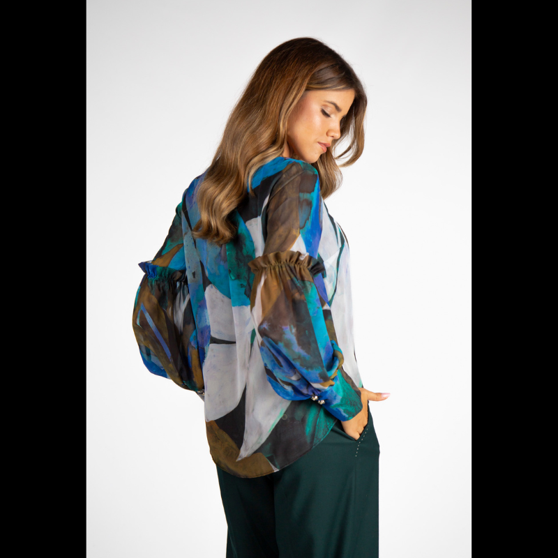 Túnica de decote em V com estampado abstrato em tons de turquesa, azul e verde. Túnica de mangas compridas em formato balão, levemente transparentes e forrada no corpo. Mangas a terminar com punho alto com dois botões metálicos em relevo.
Composição: 100%Poliester