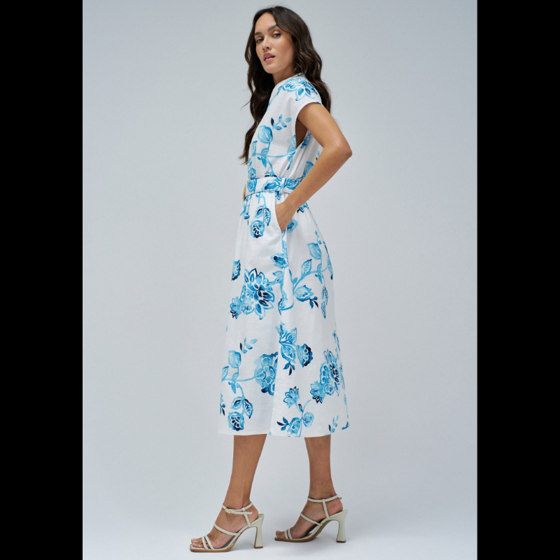 Vestido camiseiro branco com estampa floral em tons azuis. Vestido midi com decote em V e com abertura na frente com botões em madeira até à cintura. Vestido com corte na cintura com elástico e a terminar com racha frontal. Vestido de mangas cavas com bolsos laterias e com cinto removível com fivela em ráfia.
Composição: 100% Algodão
