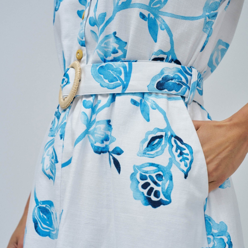 Vestido camiseiro branco com estampa floral em tons azuis. Vestido midi com decote em V e com abertura na frente com botões em madeira até à cintura. Vestido com corte na cintura com elástico e a terminar com racha frontal. Vestido de mangas cavas com bolsos laterias e com cinto removível com fivela em ráfia.
Composição: 100% Algodão