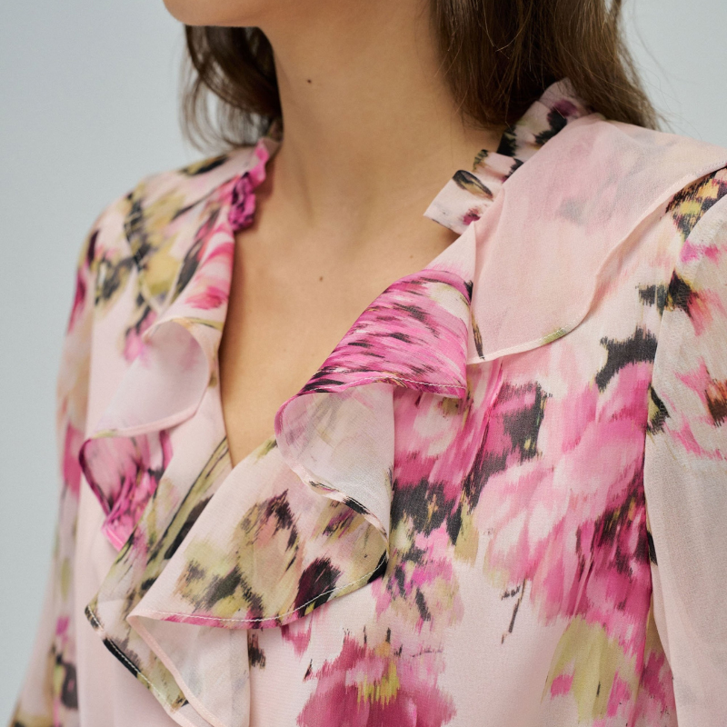 Vestido em tons rosa com padrão floral que combina elegância e movimento. O decote em V é realçado por folhos delicados, enquanto as mangas compridas apresentam punhos abotoados para um acabamento refinado. Destaca-se o cinto com pendentes nas extremidades, que adiciona dinamismo à silhueta. O folho na bainha confere volume e feminilidade. Vestido totalmente forrado para conforto e durabilidade. Uma peça versátil que transita com facilidade entre ocasiões casuais e mais sofisticadas.