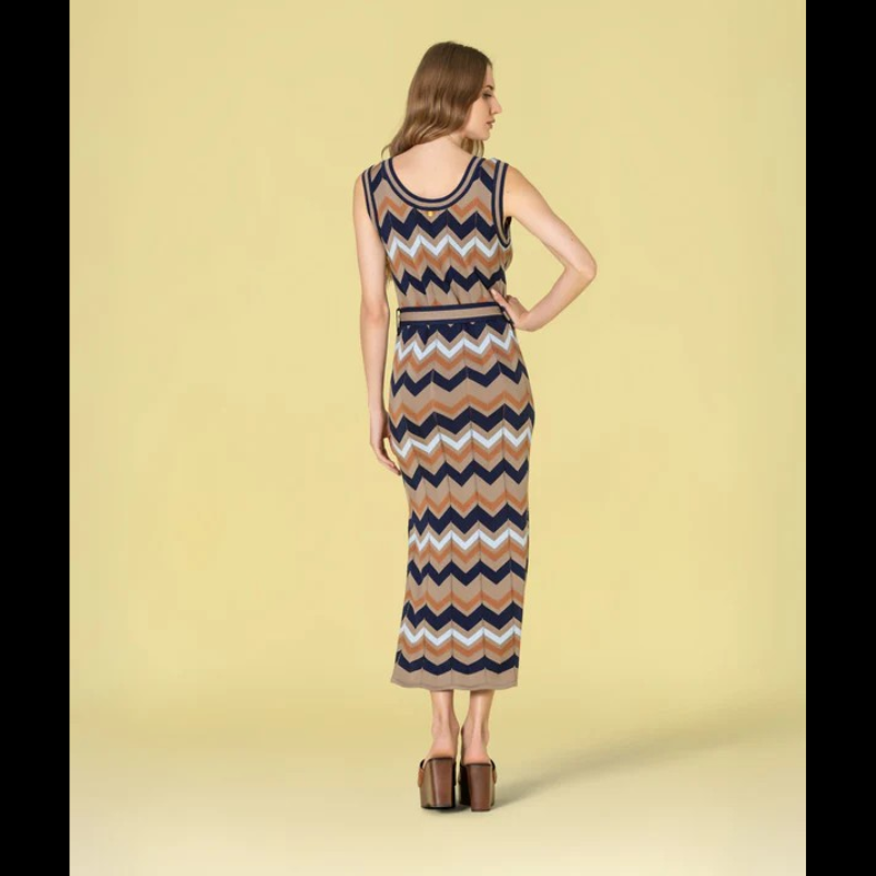 Vestido versátil em malha com decote redondo e cavas generosas, apresentando um padrão geométrico em zigzag que combina taupe, azul-marinho, azul-claro e caramelo. O corte midi é complementado por duas aberturas laterais que conferem movimento e conforto. Inclui cinto coordenado nos mesmos tons, permitindo ajustar o caimento conforme desejado. Uma escolha sofisticada para quem valoriza design contemporâneo e funcionalidade.