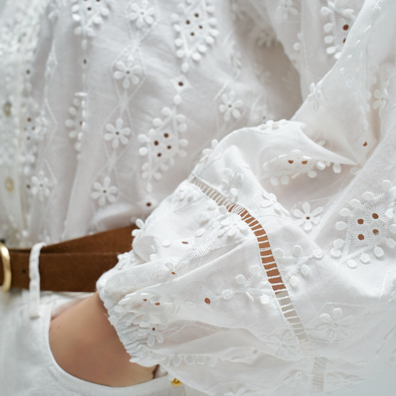 Blusa em branco com bordado em relevo e apliques florais tridimensionais que conferem textura e movimento à peça. Decote em V elegante e abertura frontal com botões para fácil ajuste. Mangas abalonadas que criam um efeito volumoso e feminino, complementadas por punhos com elástico para um acabamento confortável. Fit regular que se adapta perfeitamente ao corpo. Uma peça versátil ideal para criar looks sofisticados do dia a dia ou ocasiões especiais.