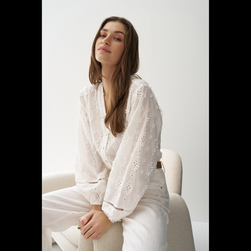 Blusa em branco com bordado em relevo e apliques florais tridimensionais que conferem textura e movimento à peça. Decote em V elegante e abertura frontal com botões para fácil ajuste. Mangas abalonadas que criam um efeito volumoso e feminino, complementadas por punhos com elástico para um acabamento confortável. Fit regular que se adapta perfeitamente ao corpo. Uma peça versátil ideal para criar looks sofisticados do dia a dia ou ocasiões especiais.