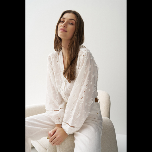 Blusa em branco com bordado em relevo e apliques florais tridimensionais que conferem textura e movimento à peça. Decote em V elegante e abertura frontal com botões para fácil ajuste. Mangas abalonadas que criam um efeito volumoso e feminino, complementadas por punhos com elástico para um acabamento confortável. Fit regular que se adapta perfeitamente ao corpo. Uma peça versátil ideal para criar looks sofisticados do dia a dia ou ocasiões especiais.