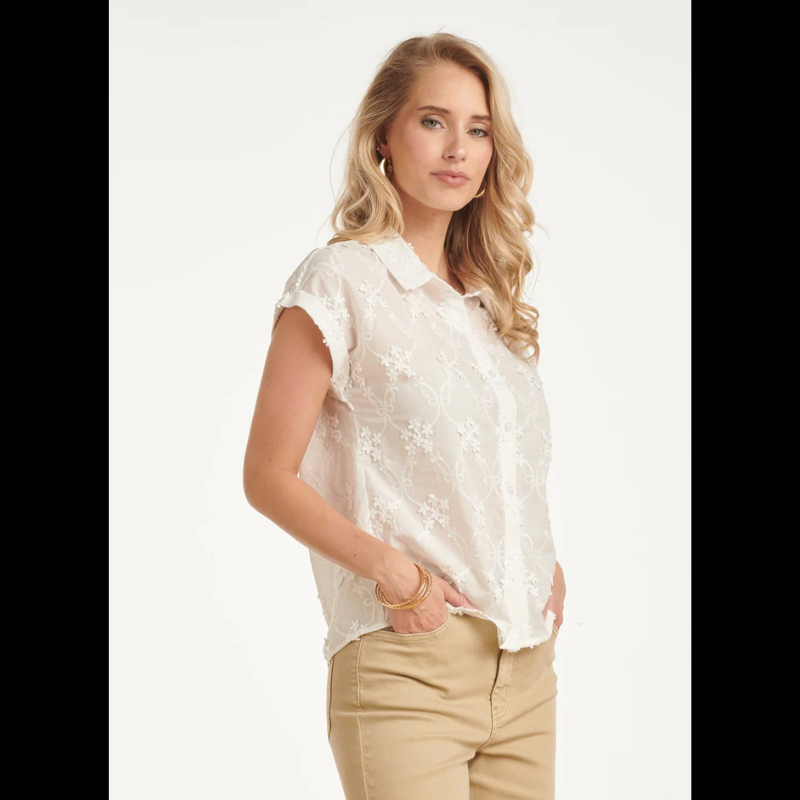 Blusa branca de manga curta, adornada com um padrão floral delicado em detalhes de bordado refinado. Fechamento frontal com botões.