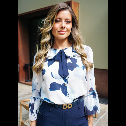 Blusa com estampado floral abstrato com padrão, em tons de azul-marinho, azul-claro e branco, confere um efeito delicado e atual ao visual. A gola com folhos traz um toque romântico, enquanto o laço azul escuro amovível no decote permite adaptar o look conforme a ocasião. Fecho frontal por botões prata e mangas compridas com punhos em folho que completam o design com requinte e feminilidade.