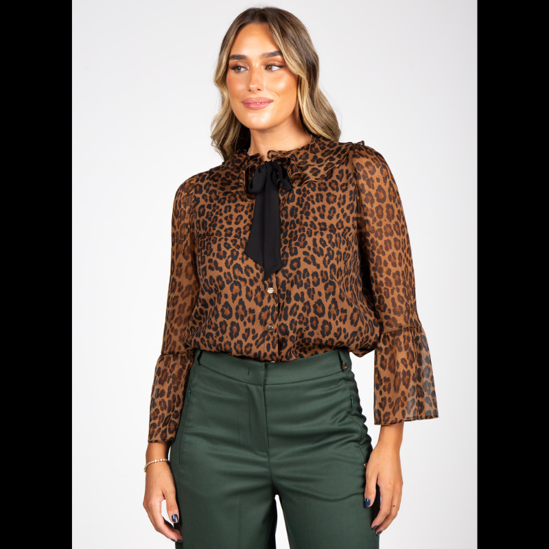 Blusa com estampado animal print de leopardo em tons de castanho, caramelo e preto que conferem profundidade e sofisticação. Confecionada em tecido leve e semitransparente com caimento fluido e elegante. A gola com folhos traz um toque romântico, enquanto o laço preto amovível no decote permite adaptar o look conforme a ocasião. Fecho frontal por botões prata e mangas compridas com punhos em folho que completam o design com requinte e feminilidade.
