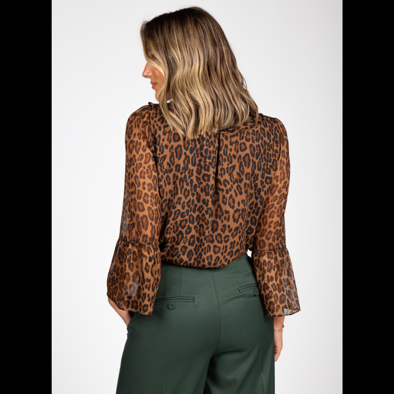 Blusa com estampado animal print de leopardo em tons de castanho, caramelo e preto que conferem profundidade e sofisticação. Confecionada em tecido leve e semitransparente com caimento fluido e elegante. A gola com folhos traz um toque romântico, enquanto o laço preto amovível no decote permite adaptar o look conforme a ocasião. Fecho frontal por botões prata e mangas compridas com punhos em folho que completam o design com requinte e feminilidade.