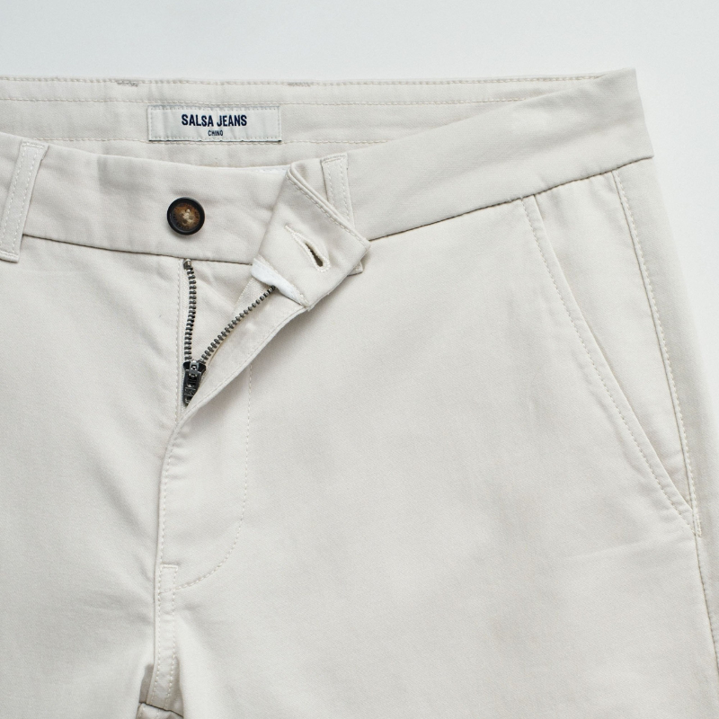 Calças chino de corte slim fit que combinam estilo e conforto. Confecionadas em tom cru neutro, apresentam cintura média com cordão interno ajustável para um encaixe personalizado. O design inclui quatro bolsos funcionais e presilhas, garantindo versatilidade no dia a dia. Ideais para criar looks casual refinados ou composições mais formais, estas calças adaptam-se facilmente a diferentes ocasiões e estilos pessoais.