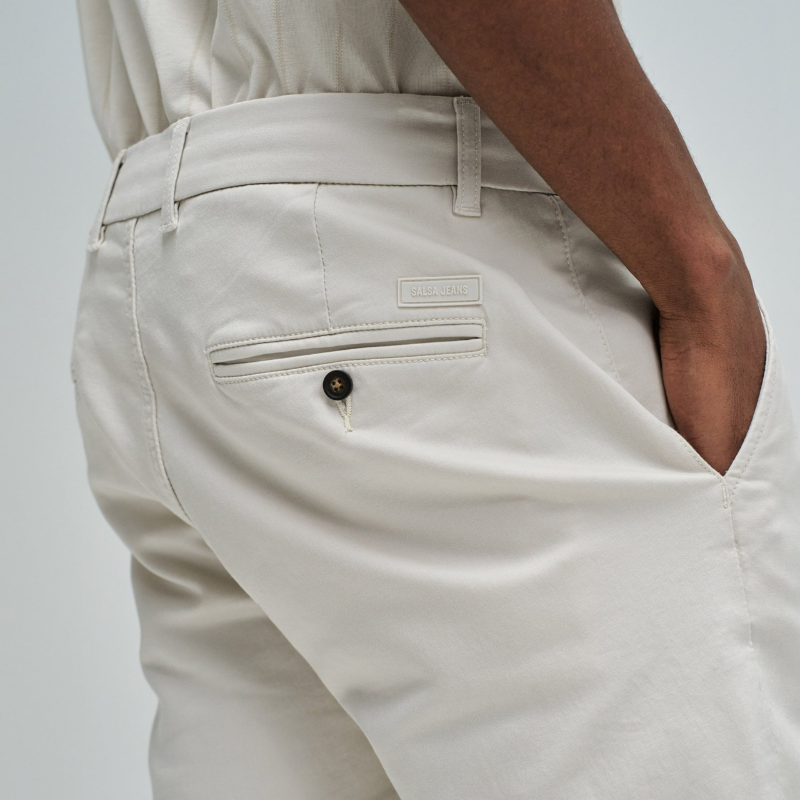 Calças chino de corte slim fit que combinam estilo e conforto. Confecionadas em tom cru neutro, apresentam cintura média com cordão interno ajustável para um encaixe personalizado. O design inclui quatro bolsos funcionais e presilhas, garantindo versatilidade no dia a dia. Ideais para criar looks casual refinados ou composições mais formais, estas calças adaptam-se facilmente a diferentes ocasiões e estilos pessoais.