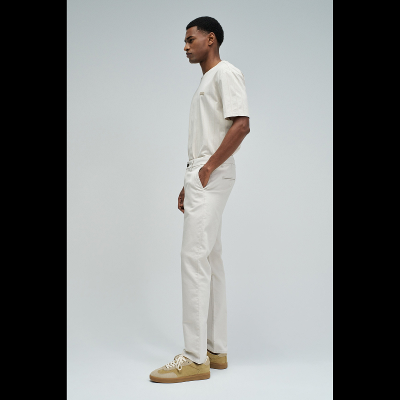 Calças chino de corte slim fit que combinam estilo e conforto. Confecionadas em tom cru neutro, apresentam cintura média com cordão interno ajustável para um encaixe personalizado. O design inclui quatro bolsos funcionais e presilhas, garantindo versatilidade no dia a dia. Ideais para criar looks casual refinados ou composições mais formais, estas calças adaptam-se facilmente a diferentes ocasiões e estilos pessoais.