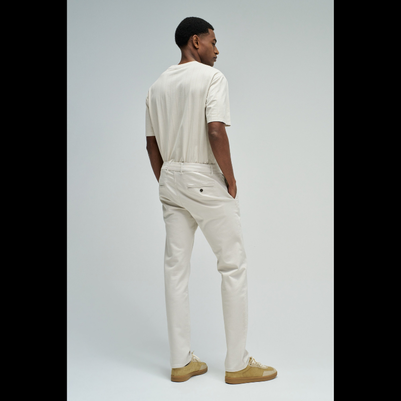 Calças chino de corte slim fit que combinam estilo e conforto. Confecionadas em tom cru neutro, apresentam cintura média com cordão interno ajustável para um encaixe personalizado. O design inclui quatro bolsos funcionais e presilhas, garantindo versatilidade no dia a dia. Ideais para criar looks casual refinados ou composições mais formais, estas calças adaptam-se facilmente a diferentes ocasiões e estilos pessoais.