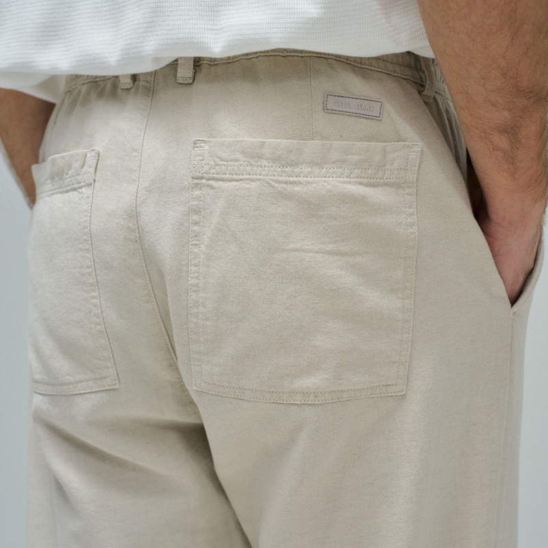 Calças joggers em algodão e linho que combinam conforto e estilo casual. O tecido natural em tom crú oferece leveza perfeita para dias quentes, enquanto a cintura média com cordão ajustável e elástico garante um encaixe seguro e confortável. Apresenta abertura com fecho de correr na cintura para facilitar o vestir, fit regular na perna e quatro bolsos funcionais. As presilhas completam o design prático e versátil, ideal para um look descontraído do dia a dia.