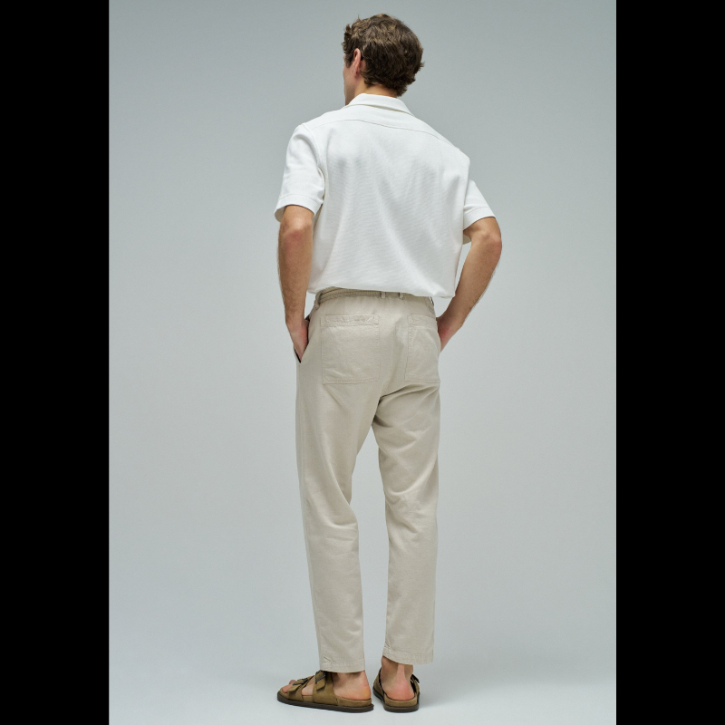 Calças joggers em algodão e linho que combinam conforto e estilo casual. O tecido natural em tom crú oferece leveza perfeita para dias quentes, enquanto a cintura média com cordão ajustável e elástico garante um encaixe seguro e confortável. Apresenta abertura com fecho de correr na cintura para facilitar o vestir, fit regular na perna e quatro bolsos funcionais. As presilhas completam o design prático e versátil, ideal para um look descontraído do dia a dia.