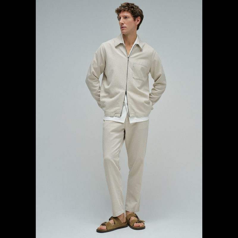 Calças joggers em algodão e linho que combinam conforto e estilo casual. O tecido natural em tom crú oferece leveza perfeita para dias quentes, enquanto a cintura média com cordão ajustável e elástico garante um encaixe seguro e confortável. Apresenta abertura com fecho de correr na cintura para facilitar o vestir, fit regular na perna e quatro bolsos funcionais. As presilhas completam o design prático e versátil, ideal para um look descontraído do dia a dia.