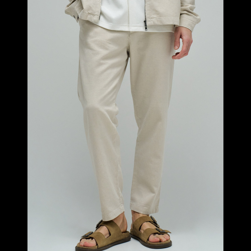 Calças joggers em algodão e linho que combinam conforto e estilo casual. O tecido natural em tom crú oferece leveza perfeita para dias quentes, enquanto a cintura média com cordão ajustável e elástico garante um encaixe seguro e confortável. Apresenta abertura com fecho de correr na cintura para facilitar o vestir, fit regular na perna e quatro bolsos funcionais. As presilhas completam o design prático e versátil, ideal para um look descontraído do dia a dia.