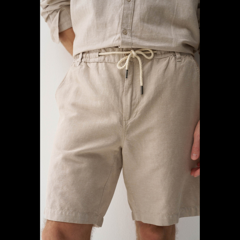 Calções em linho com um toque de sofisticação casual. O corte regular e a cintura média proporcionam conforto e elegância, enquanto o fecho de correr e botão garantem segurança. O cordão ajustável permite um ajuste personalizado conforme necessário. Quatro bolsos funcionais e presilhas completam o design prático. A cor bege neutra combina facilmente com qualquer peça do seu guarda-roupa, tornando estes calções uma escolha versátil para dias quentes.