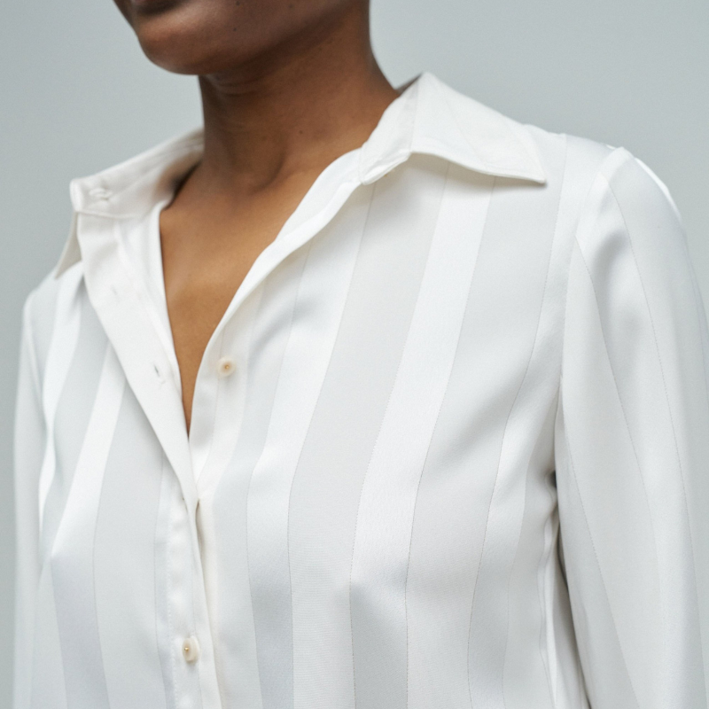 Camisa acetinada de corte regular com riscas em Lurex que adiciona um toque de sofisticação ao seu guarda-roupa. Confecionada em branco puro, apresenta mangas compridas e decote de colarinho clássico. O fecho frontal com botões e os punhos abotoados garantem um ajuste preciso e confortável. Ideal para ocasiões que exigem elegância discreta com um detalhe luminoso.