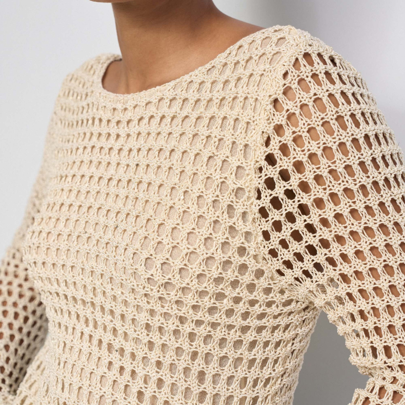 Camisola de malha elegante em bege com fios de Lurex que capturam a luz de forma subtil. Apresenta decote em barco que alarga visualmente os ombros, manga comprida e um padrão de rede com transparência estratégica que adiciona sofisticação ao visual. O fit regular oferece conforto sem apertar, ideal para looks casuais ou mais refinados. Inclui forro na parte da frente que permite usar a peça sem preocupações, garantindo discrição e funcionalidade.