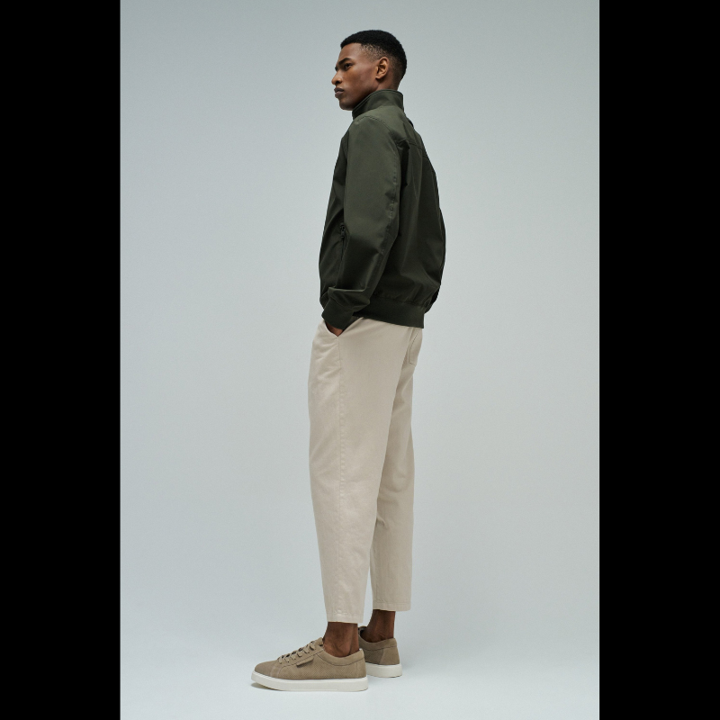 Casaco bomber em verde escuro com design versátil e funcional. Apresenta abertura frontal com fecho de correr para ajuste fácil, fit regular que se adapta confortavelmente ao corpo, e mangas compridas com punhos elásticos que garantem um acabamento limpo. Equipado com dois bolsos laterais práticos e bolso interior com fecho para maior segurança dos seus pertences. O elástico na cintura proporciona um corte definido e moderno. Uma peça essencial do guarda-roupa que combina estilo casual com funcionalidade.