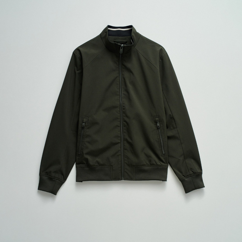 Casaco bomber em verde escuro com design versátil e funcional. Apresenta abertura frontal com fecho de correr para ajuste fácil, fit regular que se adapta confortavelmente ao corpo, e mangas compridas com punhos elásticos que garantem um acabamento limpo. Equipado com dois bolsos laterais práticos e bolso interior com fecho para maior segurança dos seus pertences. O elástico na cintura proporciona um corte definido e moderno. Uma peça essencial do guarda-roupa que combina estilo casual com funcionalidade.