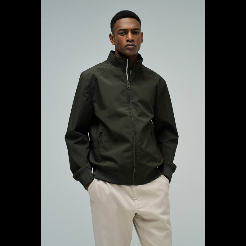 Casaco bomber em verde escuro com design versátil e funcional. Apresenta abertura frontal com fecho de correr para ajuste fácil, fit regular que se adapta confortavelmente ao corpo, e mangas compridas com punhos elásticos que garantem um acabamento limpo. Equipado com dois bolsos laterais práticos e bolso interior com fecho para maior segurança dos seus pertences. O elástico na cintura proporciona um corte definido e moderno. Uma peça essencial do guarda-roupa que combina estilo casual com funcionalidade.