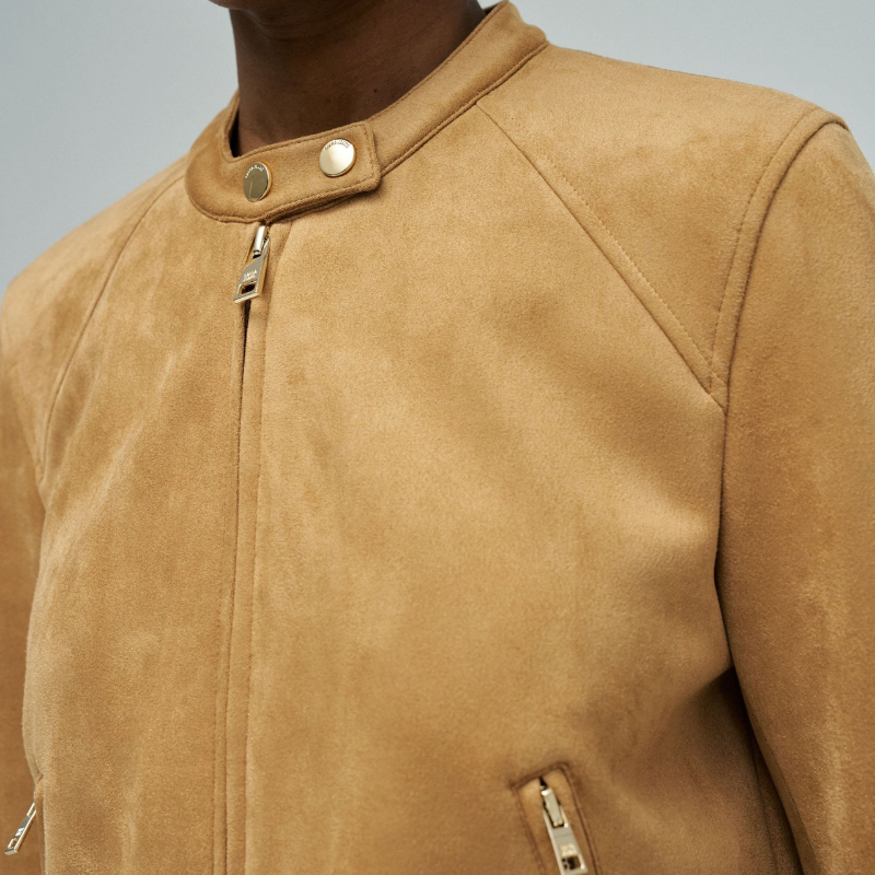 Casaco em suede camel com corte slim fit que combina elegância e conforto. Apresenta mangas compridas com fecho nos punhos para um ajuste preciso, abertura frontal com fecho de correr e decote redondo realçado por dois botões dourados de mola. Dois bolsos funcionais com fecho garantem segurança aos seus pertences. Uma peça versátil que se adapta a diversos estilos, ideal para criar looks sofisticados em qualquer estação.