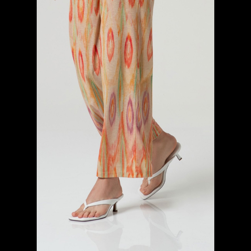 Elegantes calças pantalonas em malha fina da SURKANA, caracterizadas pela cintura média/alta com elástico na cintura que oferece conforto e ajuste seguro. O design apresenta um padrão geométrico em tons quentes de vermelho, laranja e verde sobre base bege, enriquecido com detalhes em Lurex dourado que conferem sofisticação e brilho. Peça versátil ideal para composições contemporâneas.