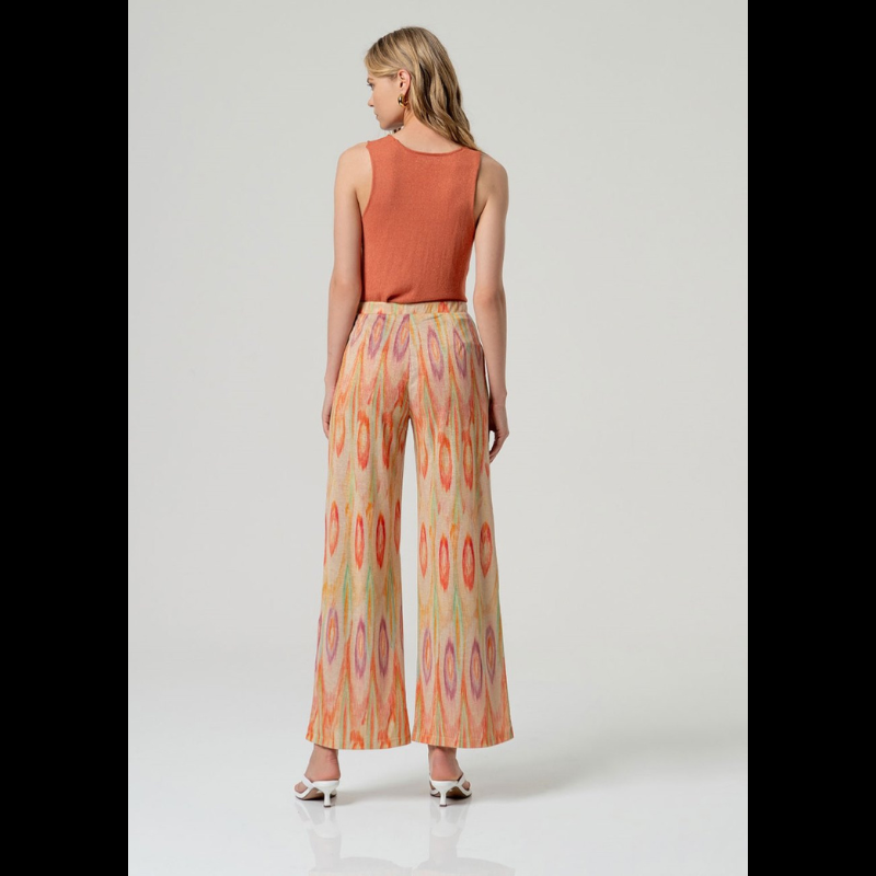 Elegantes calças pantalonas em malha fina da SURKANA, caracterizadas pela cintura média/alta com elástico na cintura que oferece conforto e ajuste seguro. O design apresenta um padrão geométrico em tons quentes de vermelho, laranja e verde sobre base bege, enriquecido com detalhes em Lurex dourado que conferem sofisticação e brilho. Peça versátil ideal para composições contemporâneas.