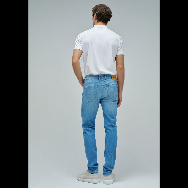 Calças jeans slim fit em azul claro com cintura média e perna ajustada. Apresenta abertura com botões, cinco bolsos funcionais e presilhas para cinto. Corte moderno que realça a silhueta, ideal para um visual casual e versátil no dia a dia.