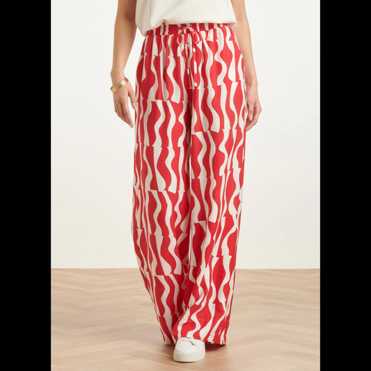 Calças largas com estampa ondulada em vermelho e branco que combinam conforto e estilo. Cintura elástica com atilho ajustável para um encaixe perfeito. Bolsos funcionais para praticidade do dia a dia. Peça versátil que funciona tanto em looks casuais como em composições mais descontraídas.