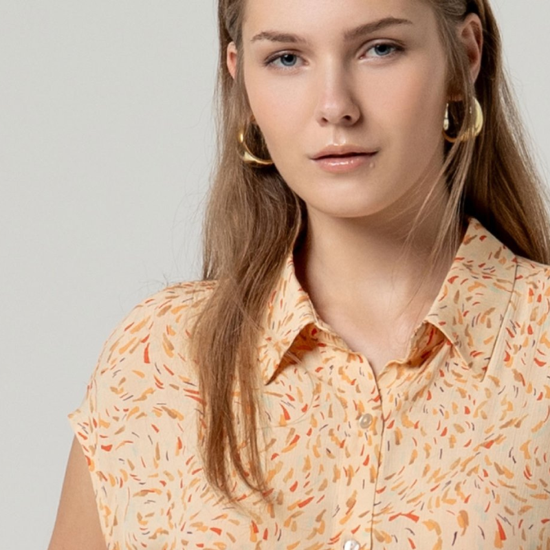 Camisa sem mangas SURKANA em tom areia com padrão vibrante em laranja, vermelho e castanho. Fechamento frontal com botões para um ajuste personalizado. Corte solto e leve, perfeito para dias quentes, com prega-macho na parte de trás que proporciona conforto e movimento. Uma peça versátil para criar looks descontraídos e elegantes.