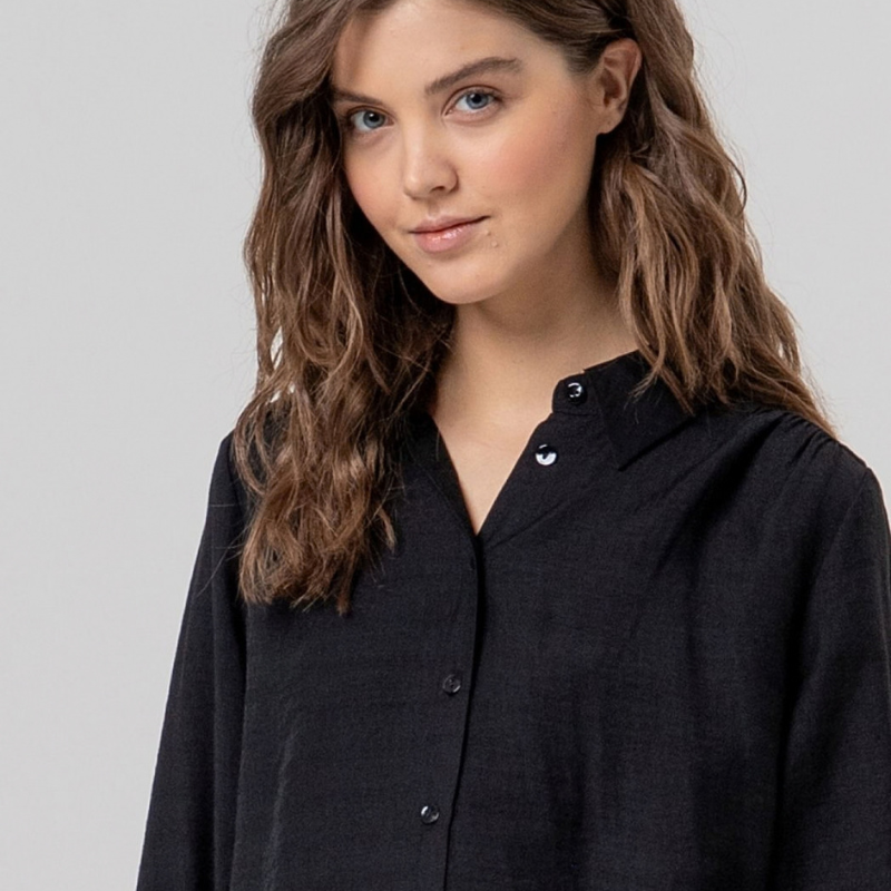 Camisa de manga comprida em preto fluida com gola e botões na frente. Ombros com franzidos que dão volume e punhos bufantes. Tecido leve com toque suave e queda limpa.