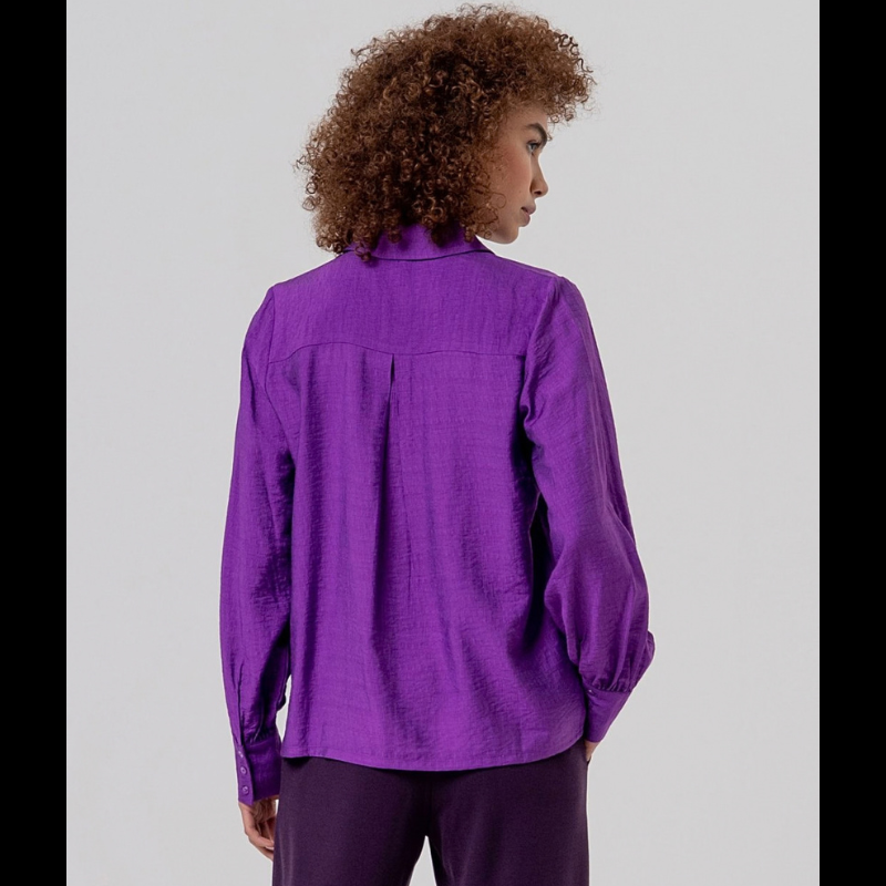 Camisa de manga comprida, em roxo, fluida com gola e botões na frente. Ombros com franzidos que dão volume e punhos bufantes.