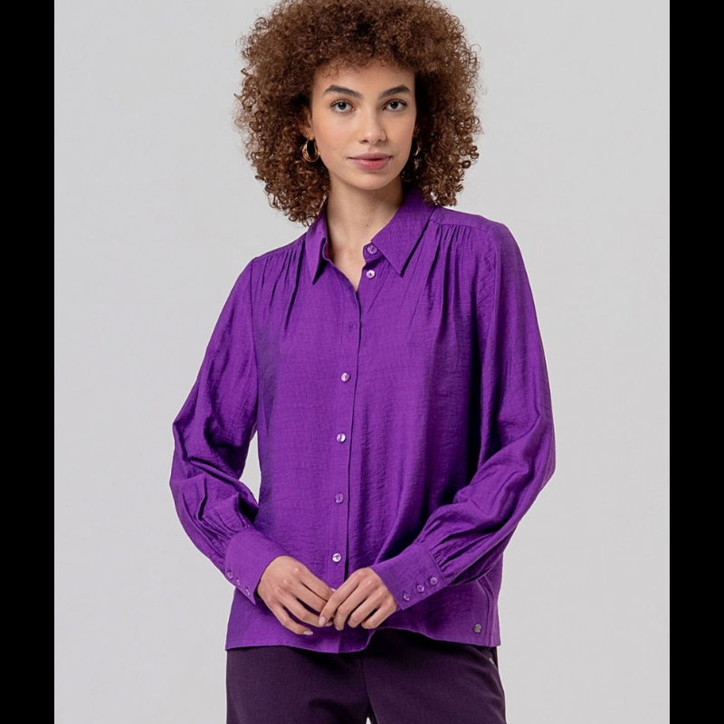 Camisa de manga comprida, em roxo, fluida com gola e botões na frente. Ombros com franzidos que dão volume e punhos bufantes.