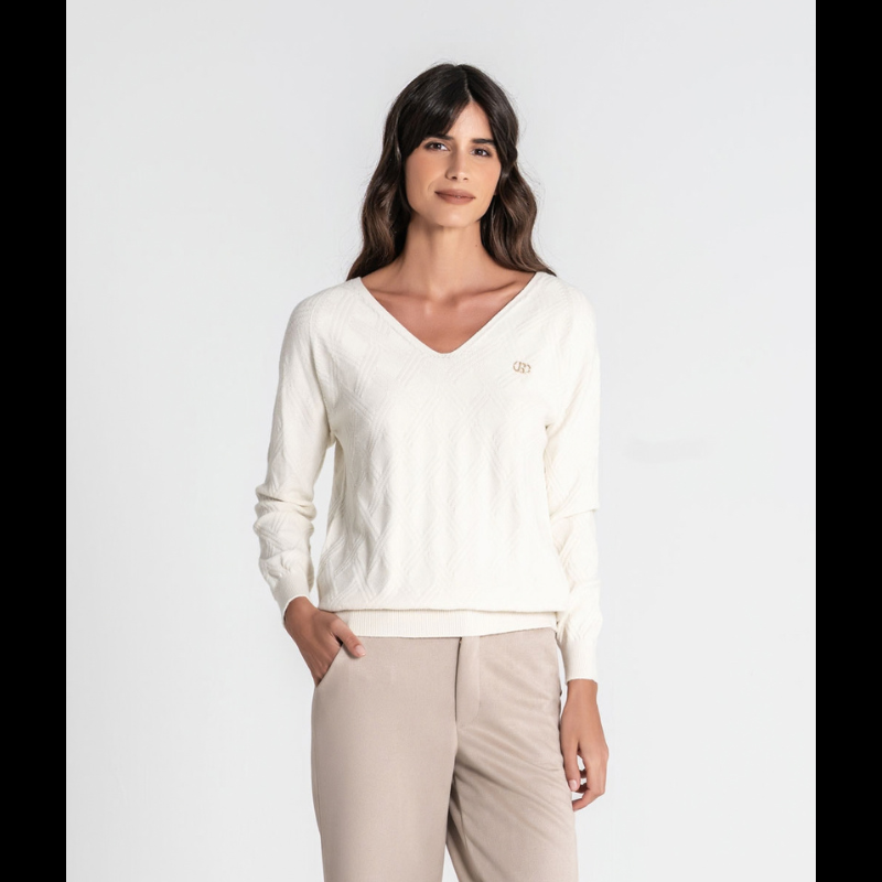 Camisola de malha fofinha com manga comprida e decote em V. Apresenta uma textura em relevo de losangos que confere profundidade e elegância ao design. A marca é destacada pela aplicação da chapa R em dourado no peito, um toque sofisticado que valoriza qualquer look. 