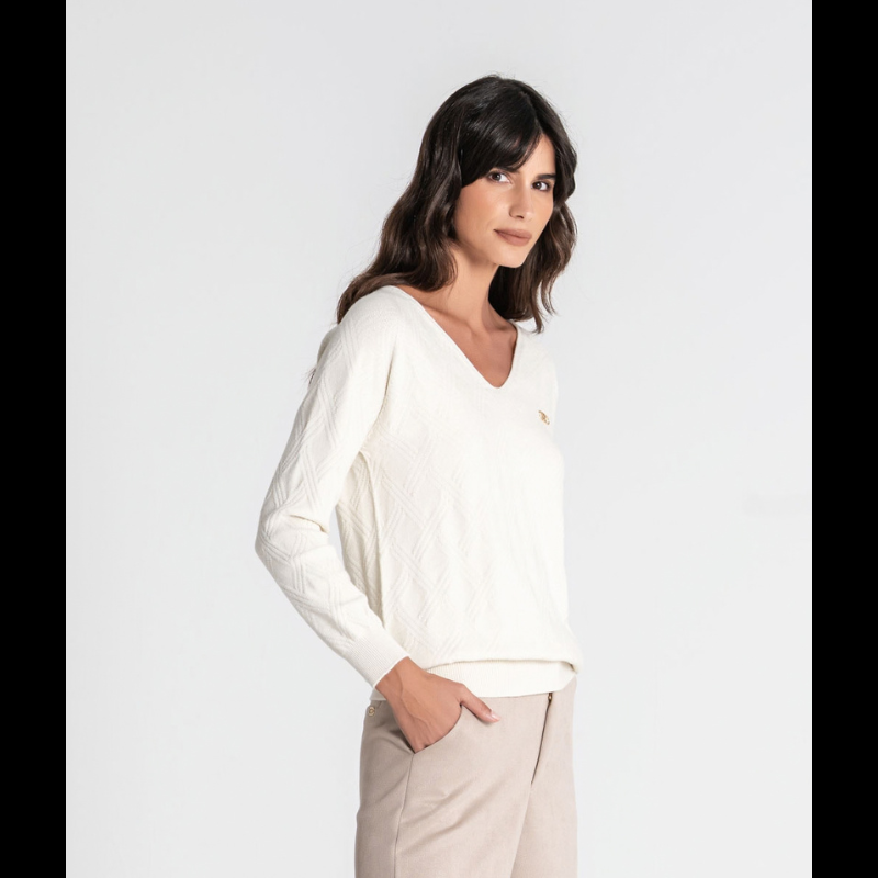 Camisola de malha fofinha com manga comprida e decote em V. Apresenta uma textura em relevo de losangos que confere profundidade e elegância ao design. A marca é destacada pela aplicação da chapa R em dourado no peito, um toque sofisticado que valoriza qualquer look. 