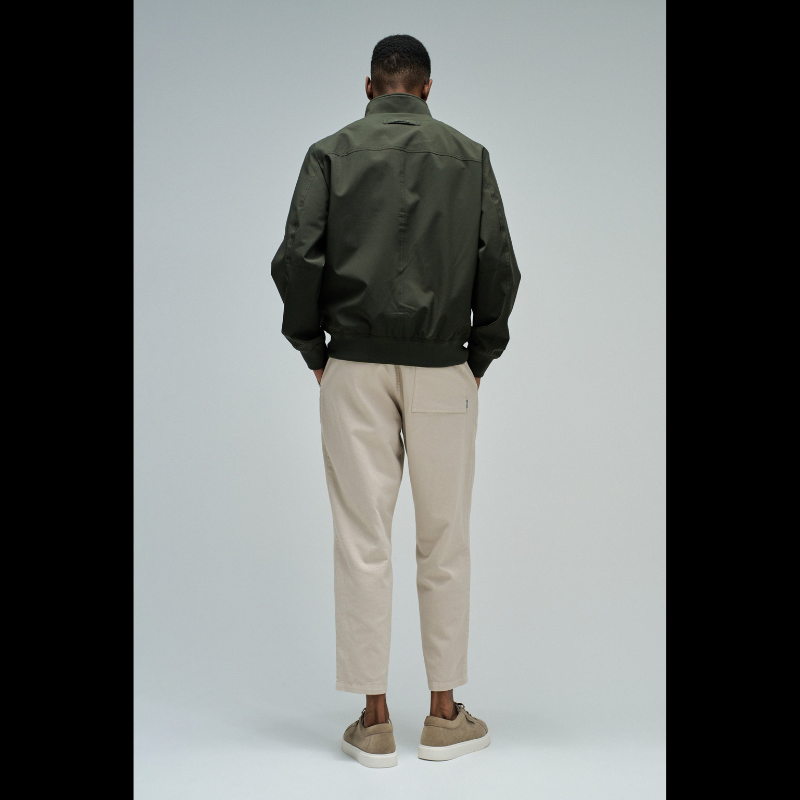 Casaco bomber em verde escuro com design versátil e funcional. Apresenta abertura frontal com fecho de correr para ajuste fácil, fit regular que se adapta confortavelmente ao corpo, e mangas compridas com punhos elásticos que garantem um acabamento limpo. Equipado com dois bolsos laterais práticos e bolso interior com fecho para maior segurança dos seus pertences. O elástico na cintura proporciona um corte definido e moderno. Uma peça essencial do guarda-roupa que combina estilo casual com funcionalidade.