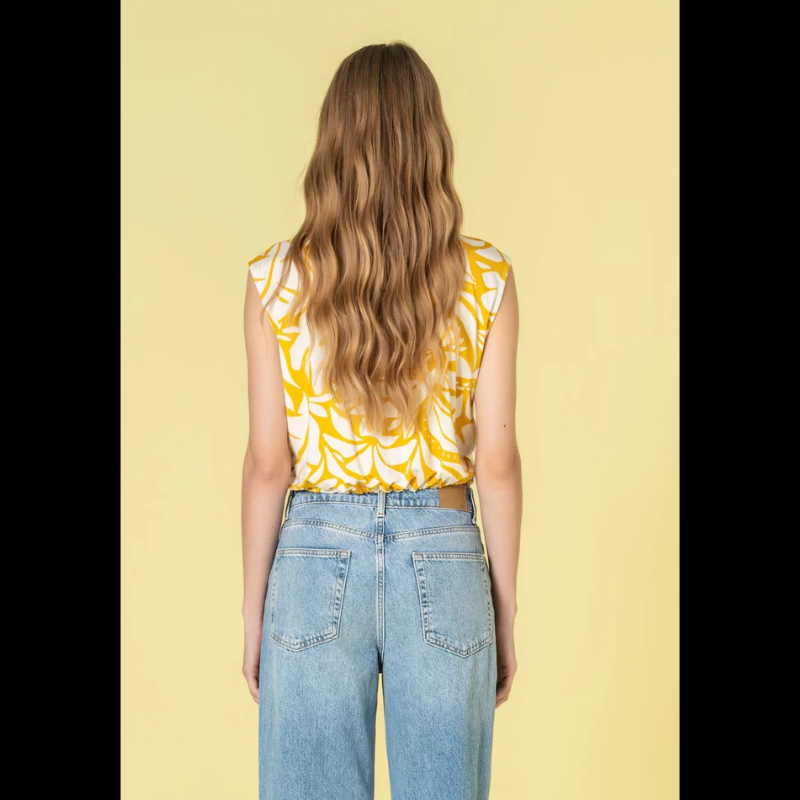 Colete versátil em tons quentes de bege e amarelo, com um padrão floral delicado que traz movimento e personalidade a qualquer look. O decote com gola a padre confere sofisticação, enquanto os botões dourados adicionam um toque de luxo. A cintura ajustável com elástico permite um ajuste personalizado para máximo conforto. Os bolsos funcionais de chapa com pala no peito combinam praticidade com estilo, tornando este colete tanto elegante quanto versátil para o dia a dia.