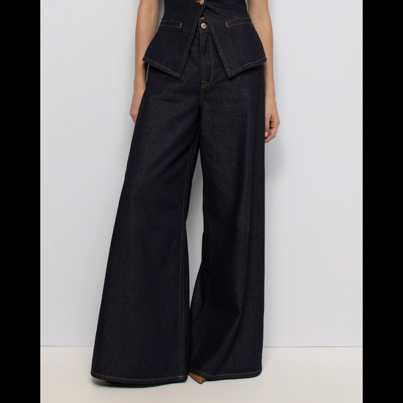 Calças jeans super wide leg em denim azul escuro com cintura muito alta. Corte generoso na perna que oferece conforto e estilo contemporâneo. Detalhes funcionais incluem abertura frontal com fecho e botão, cinco bolsos espaçosos e presilhas