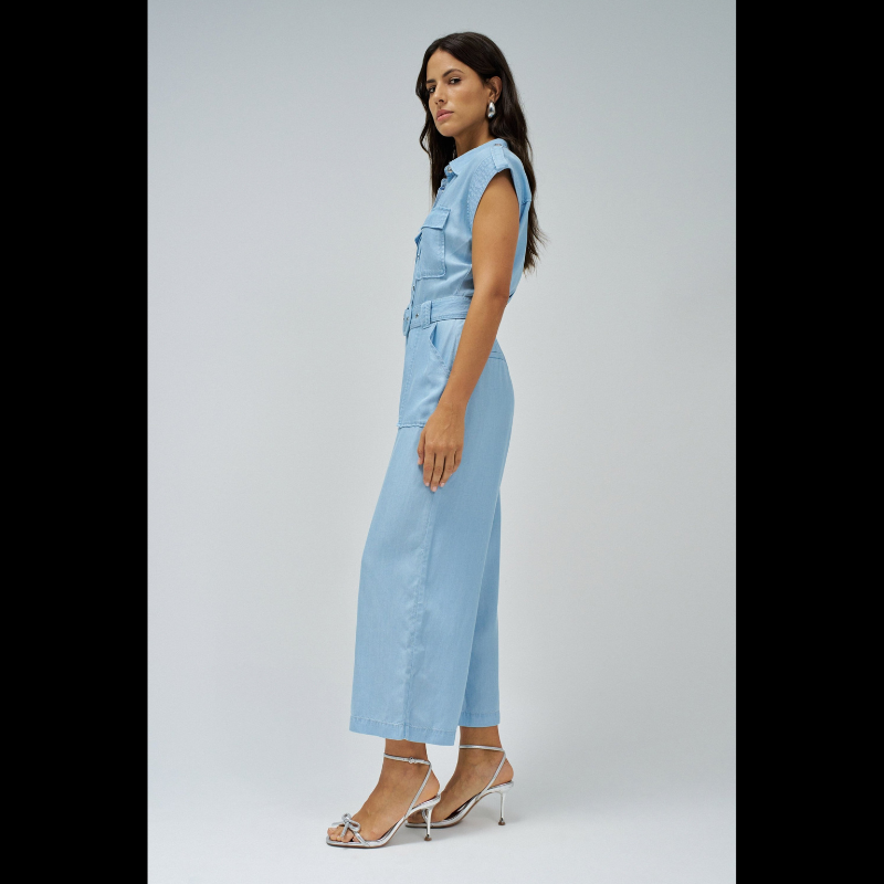 Macacão versátil em lightdenim azul claro que combina estilo casual com funcionalidade. Apresenta decote de colarinho clássico e mangas curtas, ideal para dias quentes. A silhueta cropped slim na perna oferece um visual moderno e ajustado. Fechamento prático com botões e fecho frontal, complementado por um cinto removível que permite ajustar o caimento conforme deseja. Seis bolsos estrategicamente posicionados — dois no peito, dois frontais funcionais e dois traseiros decorativos — garantem espaço para o es