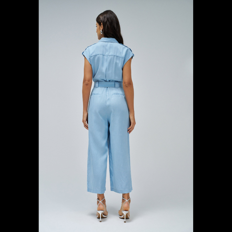 Macacão versátil em lightdenim azul claro que combina estilo casual com funcionalidade. Apresenta decote de colarinho clássico e mangas curtas, ideal para dias quentes. A silhueta cropped slim na perna oferece um visual moderno e ajustado. Fechamento prático com botões e fecho frontal, complementado por um cinto removível que permite ajustar o caimento conforme deseja. Seis bolsos estrategicamente posicionados — dois no peito, dois frontais funcionais e dois traseiros decorativos — garantem espaço para o es