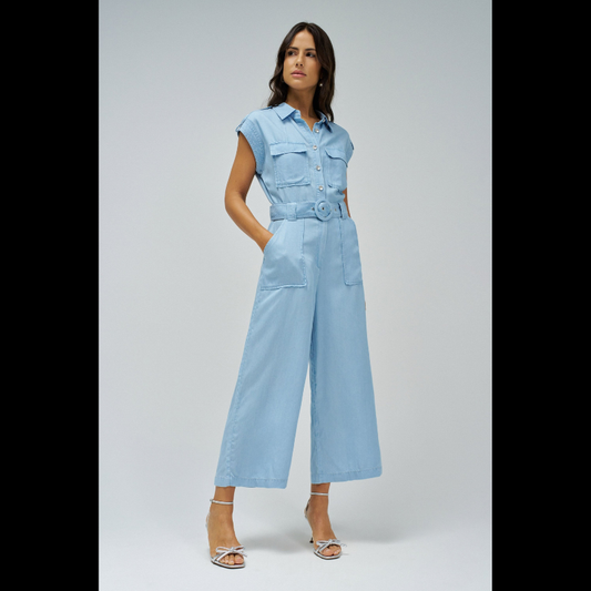 Macacão versátil em lightdenim azul claro que combina estilo casual com funcionalidade. Apresenta decote de colarinho clássico e mangas curtas, ideal para dias quentes. A silhueta cropped slim na perna oferece um visual moderno e ajustado. Fechamento prático com botões e fecho frontal, complementado por um cinto removível que permite ajustar o caimento conforme deseja. Seis bolsos estrategicamente posicionados — dois no peito, dois frontais funcionais e dois traseiros decorativos — garantem espaço para o es