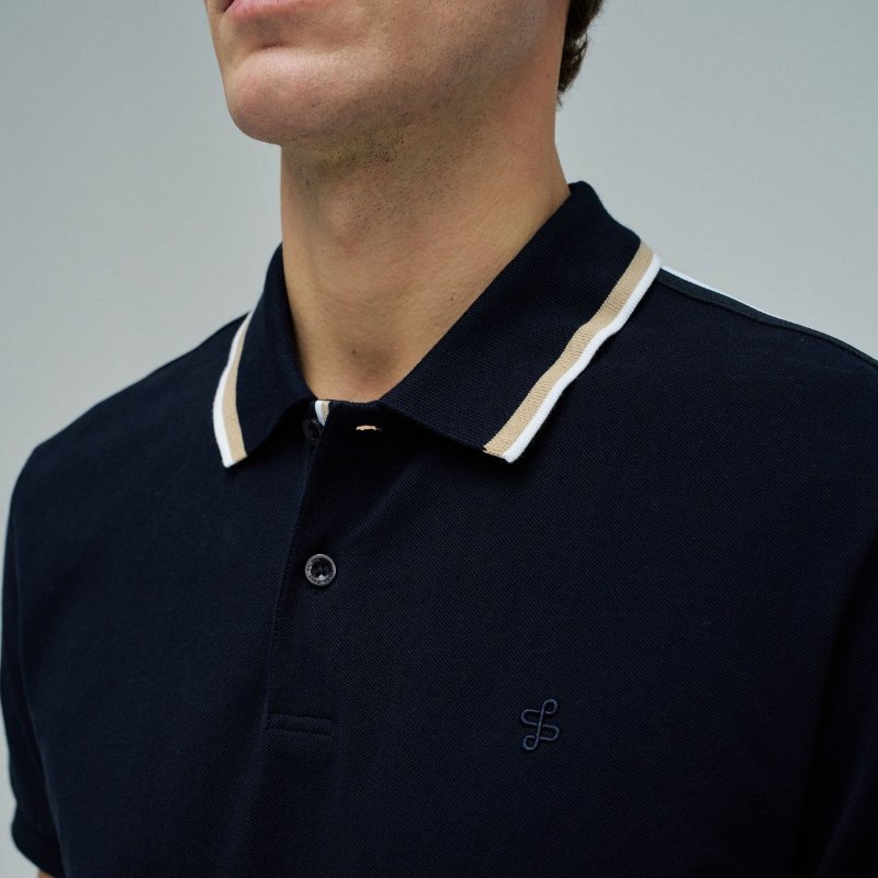 Polo clássico em Marinho com fit regular e mangas curtas. Apresenta decote de colarinho com botões e detalhe de riscas no colarinho que adiciona um toque de sofisticação. Perfeito para um visual casual e versátil, combina conforto com estilo contemporâneo. Ideal para o dia a dia ou ocasiões mais descontraídas.