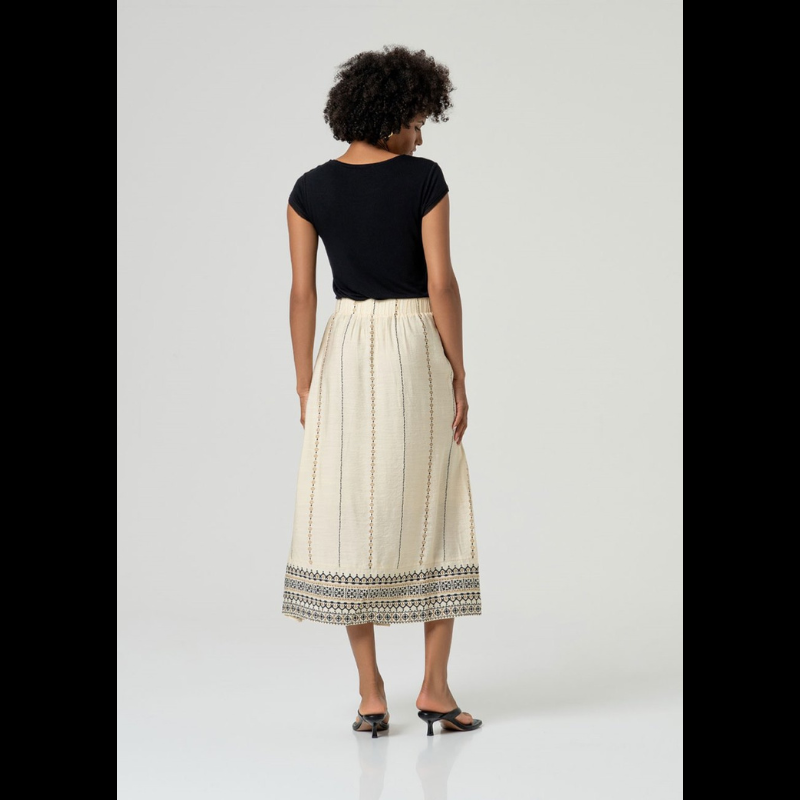 Saia maxi em crú/areia com bordado geométrico estampado em preto e camel que percorre a vertical e a faixa. Apresenta pregas na frente, elástico na cintura traseira e bolsos laterais funcionais. Fecho invisível na lateral garante um acabamento limpo e elegante. Confecionada em viscose e poliamida e com forro, que lhe oferece conforto e fluidez no movimento.